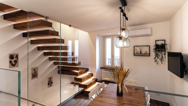 Un intérieur moderne avec un escalier en bois, un coin repas doté d’une table en verre et un luminaire fixé au plafond.