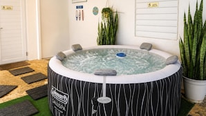 A hot tub with a Coleman logo, surrounded by potted plants, a sign for a slippery floor, and a door with a doormat. - Casita Blue Surfer-Luquillo 15 minutes to El Yunque, and 3 minutes to the beach (Luquillo)