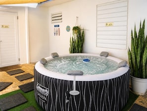 A hot tub with a Coleman logo, surrounded by potted plants, a sign for a slippery floor, and a door with a doormat. - Casita Blue Surfer-Luquillo 15 minutes to El Yunque, and 3 minutes to the beach (Luquillo)