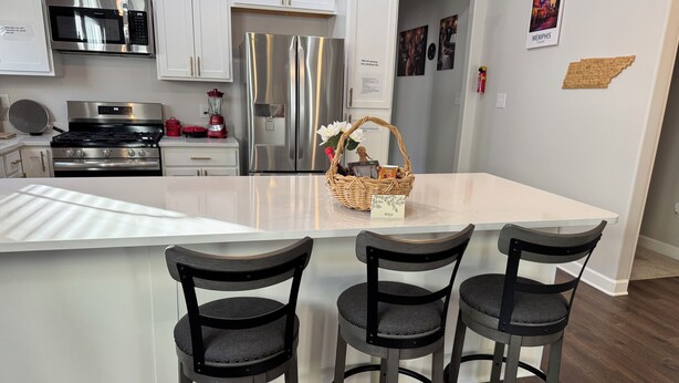 A modern kitchen with white cabinets, stainless steel appliances, and a central island with bar stools. - Family-Friendly Free Parking, Drinks & Snacks all complementary (Memphis)