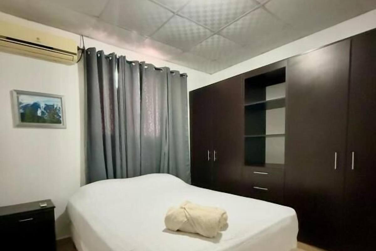 A bedroom with a bed, dark wooden wardrobe, and a small bedside table.