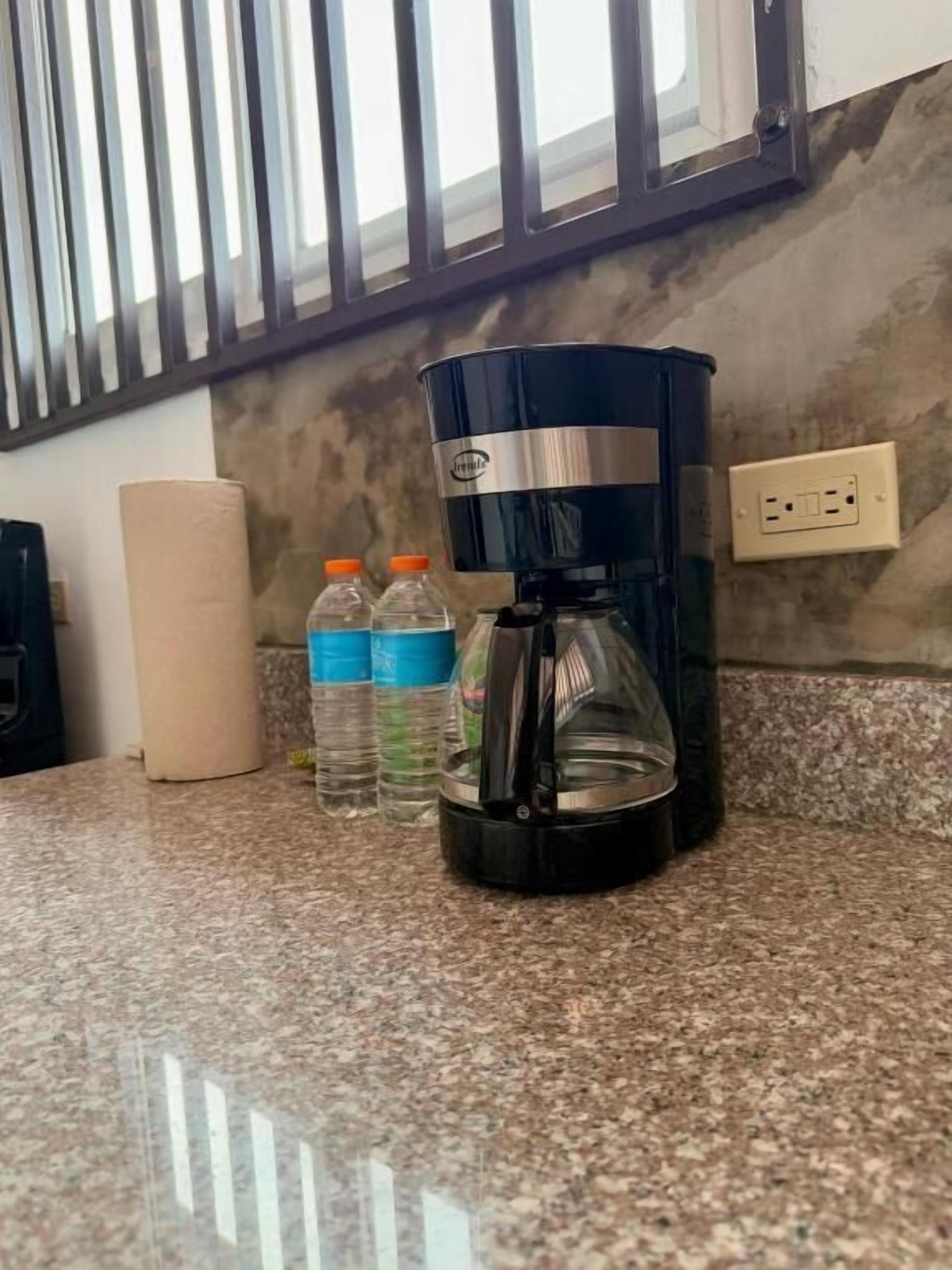A kitchen with a coffee maker, two water bottles, and a roll of paper towels on the counter.