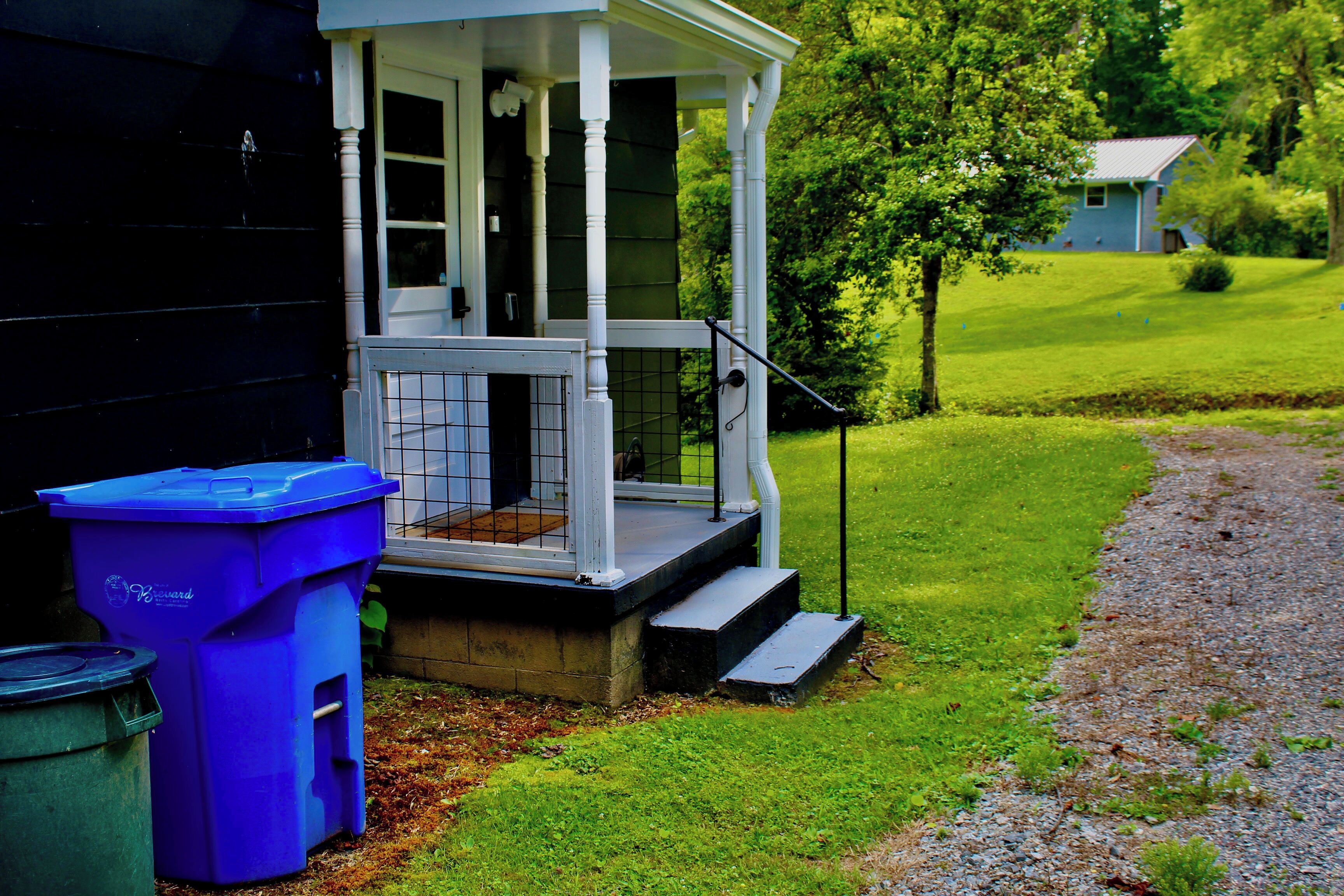 A house with a porch, a trash bin, and a grassy yard.