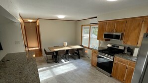 Eine Küche mit Granit-Arbeitsplatten, einem Essbereich mit Tisch und Stühlen, Holzschränken und einem Edelstahl-Kühlschrank.