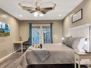 A bedroom with a bed, a desk, a chair, a ceiling fan, and a window with curtains.