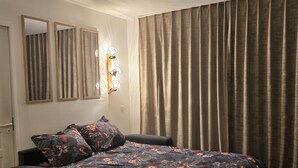 A bedroom with a bed, two wall-mounted mirrors, a wall-mounted light fixture, and a window with curtains. - Apartment with kitchenette in the mountains of Valmeinier  (Valmeinier)