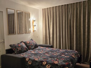 A bedroom with a bed, two wall-mounted mirrors, a wall-mounted light fixture, and a window with curtains. - Apartment with kitchenette in the mountains of Valmeinier  (Valmeinier)