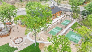 Ett utomhusområde för rekreation med en eldstad, tennisbanor och en byggnad med stora fönster.