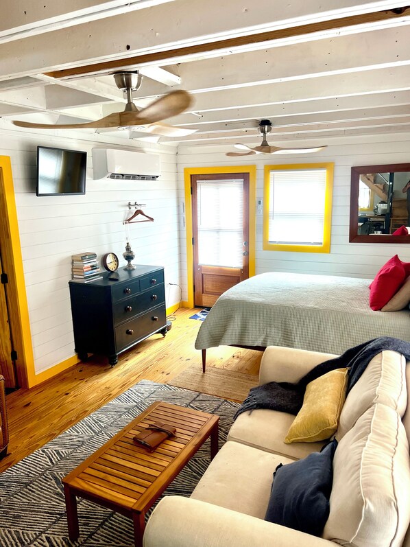 A room with a bed, a sofa, a wooden coffee table, a dresser, a television, and a ceiling fan.