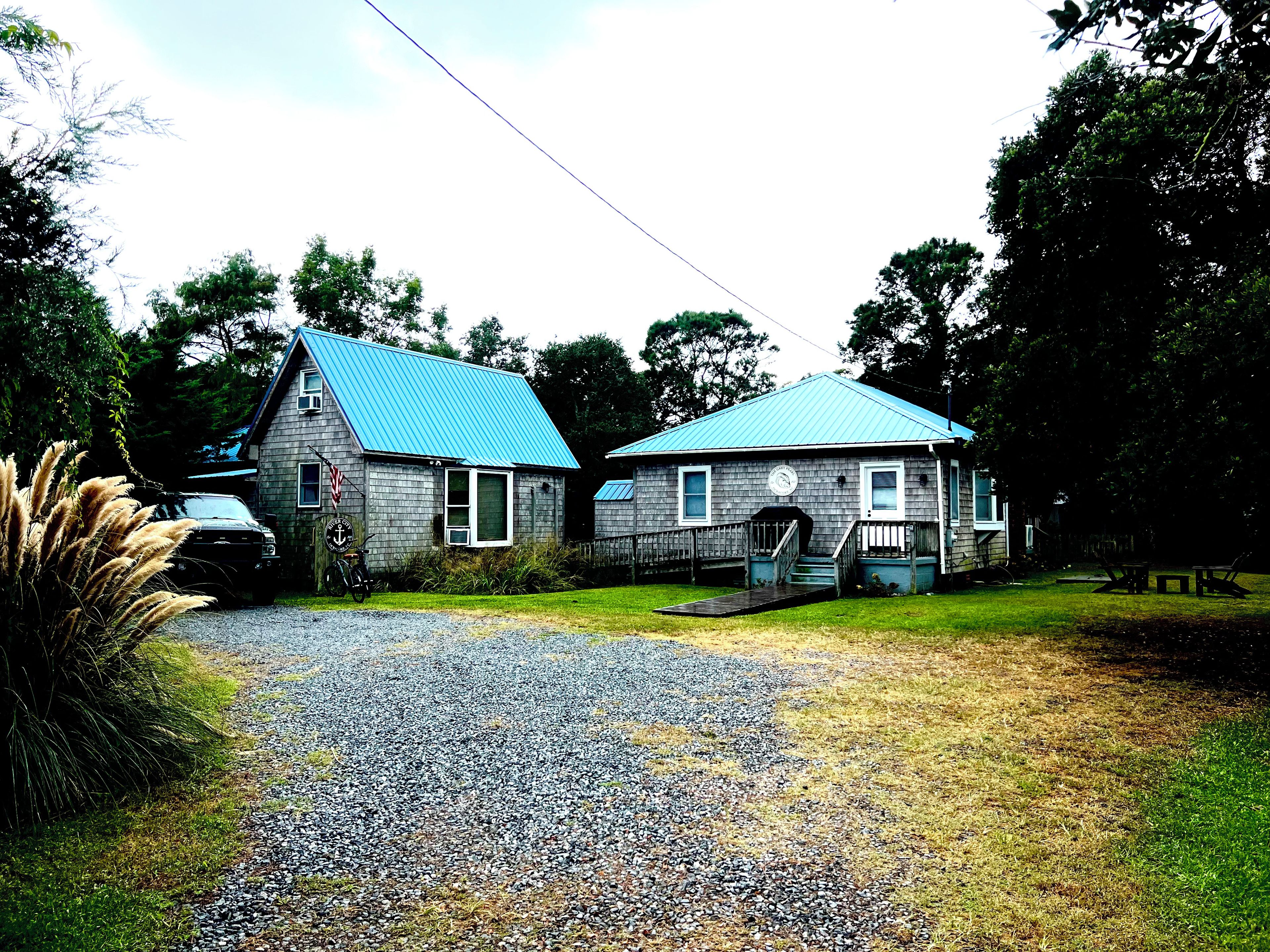 A two-story building with a blue roof, a front porch, and a gravel driveway.
