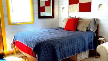 A bedroom with a wooden ceiling, a bed with a blue quilt, a red pillow, and a flag on the wall.