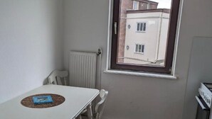 A small kitchen with a window, a table with chairs, and a radiator. - 2 room apartment (Bremen)