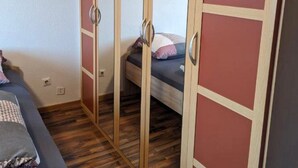 A bedroom with a bed, a wardrobe with mirrored doors, and a wooden floor. - 2 room apartment (Bremen)