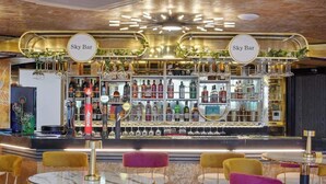 Un espace bar agrémenté de deux enseignes « Sky Bar », d’une variété de bouteilles d’alcool et de plusieurs types de sièges, avec des tables et des chaises rondes.