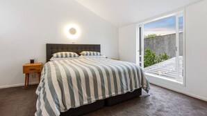 Un dormitorio con cama, mesita de noche, lámpara de pared y puerta corredera de cristal que da a un espacio exterior.