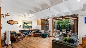 Amplia sala de estar con piso de madera, sofás de cuero, comedor con mobiliario para exteriores y un gran ventanal con vista a zonas verdes.