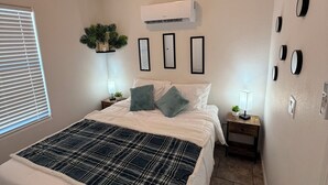 A bedroom with a large bed, an air conditioner, a nightstand with a lamp, and a wall-mounted clock. - River Lagoon #82 Access to the Colorado River (Ehrenberg)