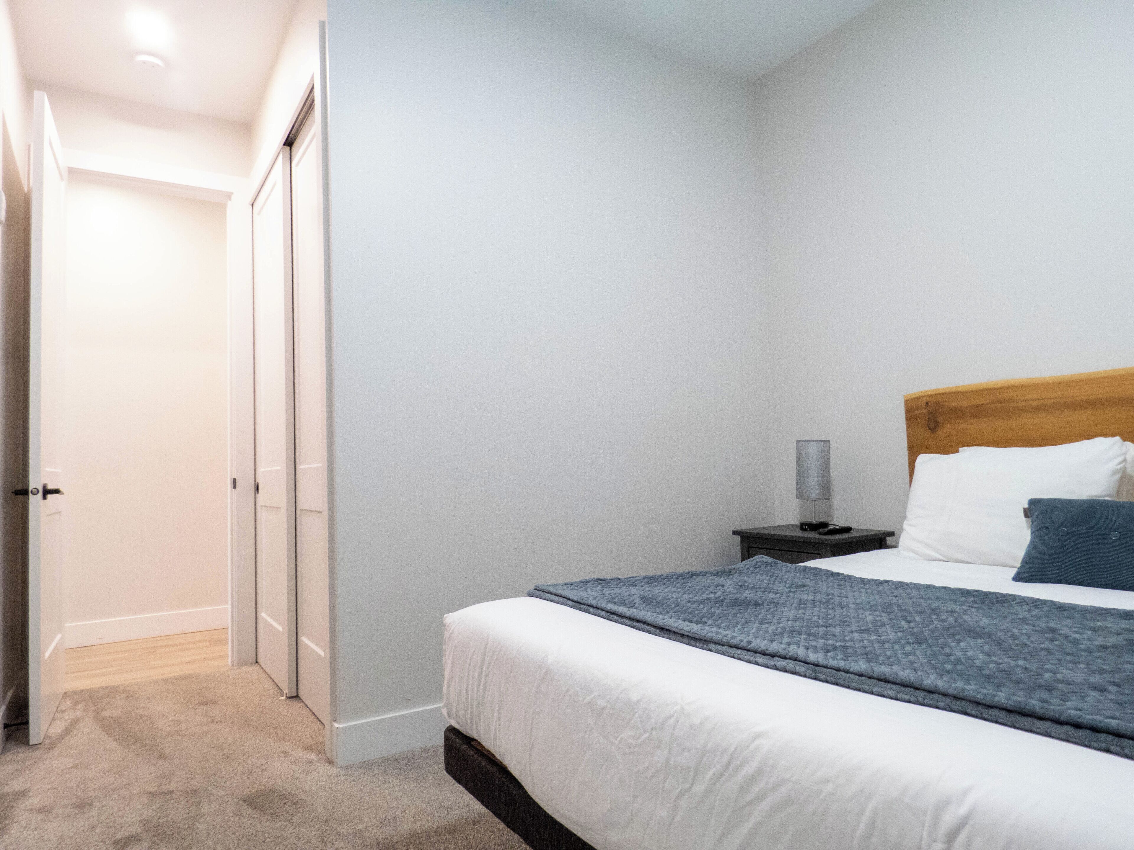 Een slaapkamer met een bed, nachtkastje, lamp en een deur naar een andere kamer.