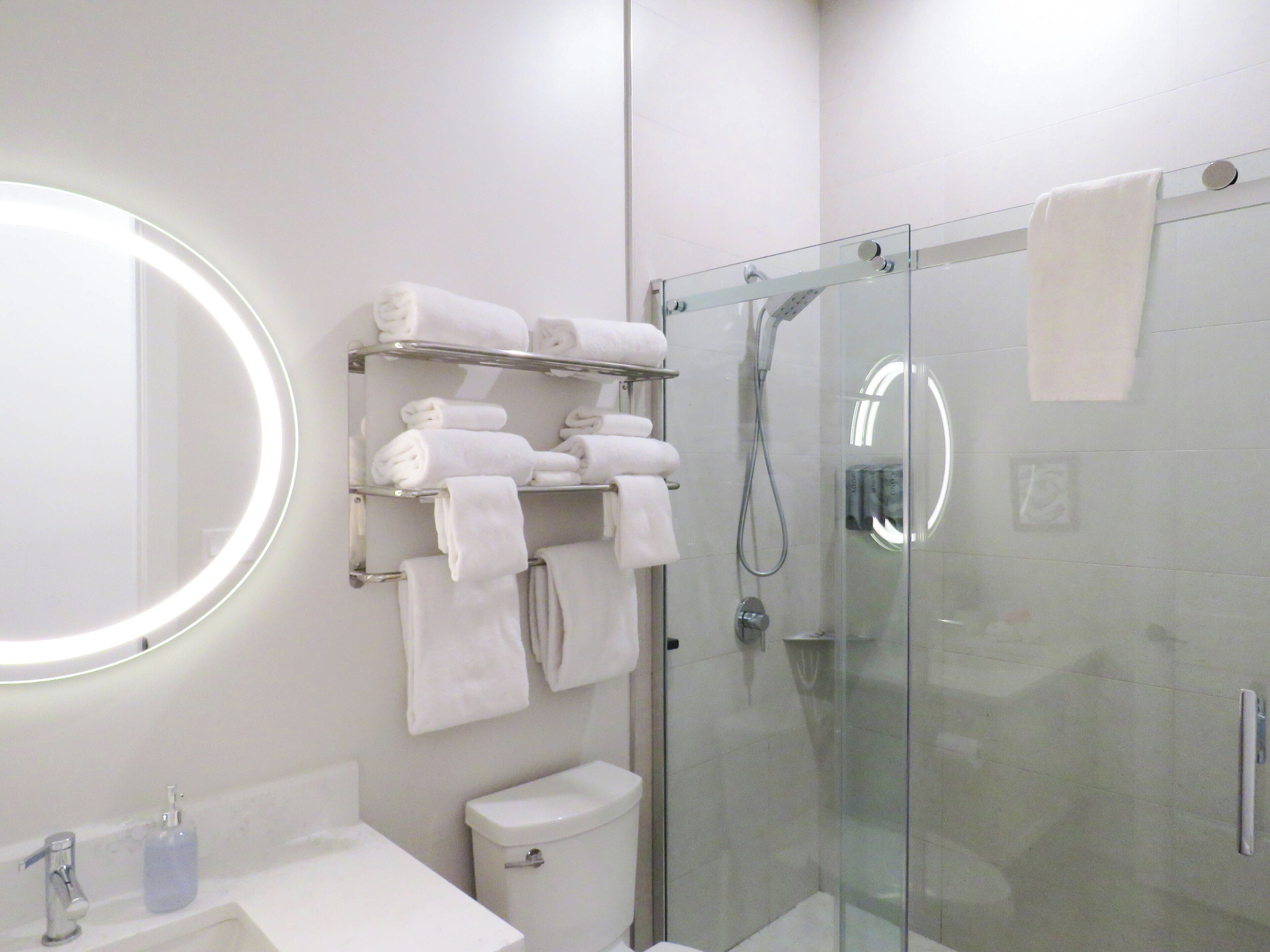A modern bathroom with a glass-enclosed shower, a toilet, a sink with a mirror, and a towel rack with neatly folded towels.