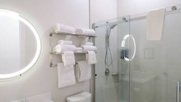 A modern bathroom with a glass-enclosed shower, a toilet, a sink with a mirror, and a towel rack with neatly folded towels.