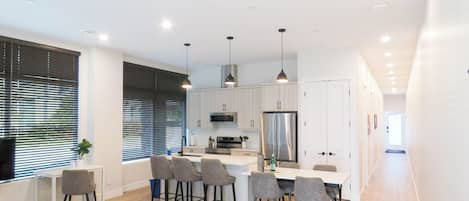 A modern kitchen with white cabinets, a stainless steel refrigerator, and a dining area with grey chairs.