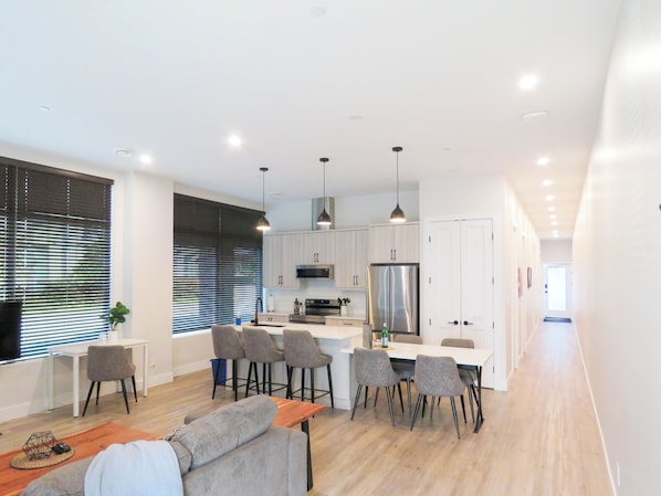 A modern kitchen with white cabinets, a stainless steel refrigerator, and a dining area with grey chairs.