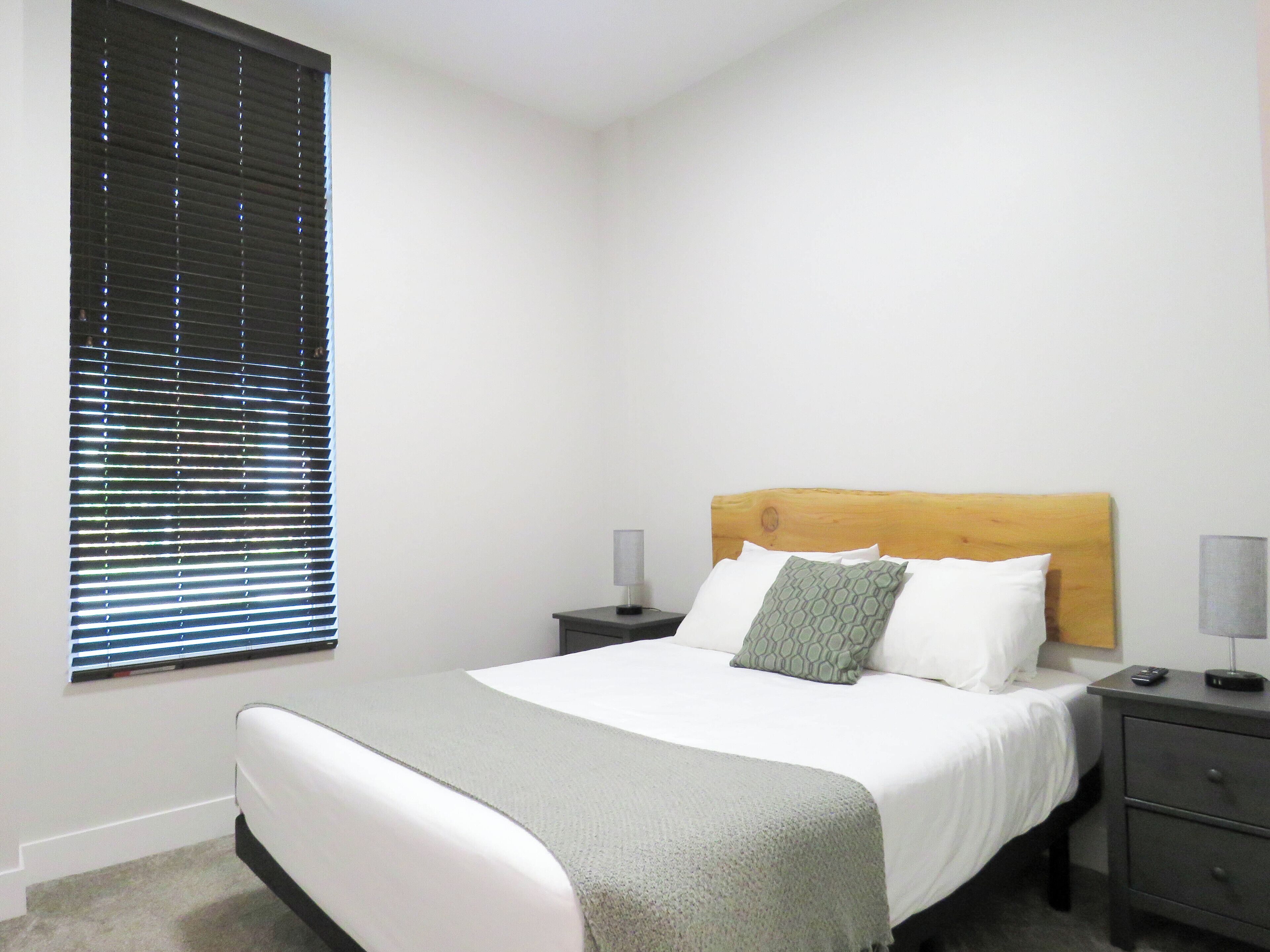 A bedroom with a bed, a wooden headboard, two bedside tables, and a window with blinds.