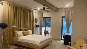 A bedroom with a bed, a ceiling fan, a desk, a chair, and a view of the outdoors.