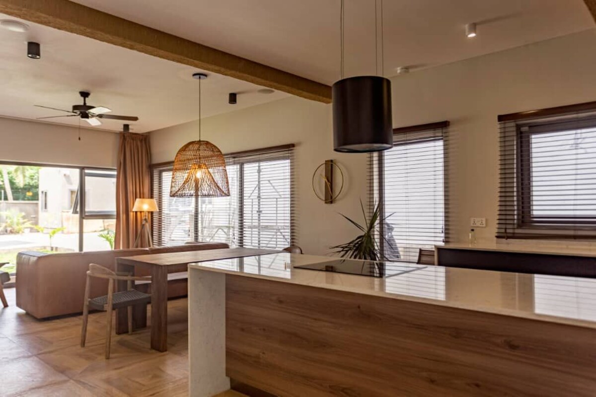 A modern kitchen with a wooden island, pendant lighting, and large windows with blinds.