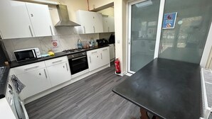 A modern kitchen with white cabinets, a microwave, stove, and a fire extinguisher. - Gassiot House (London)