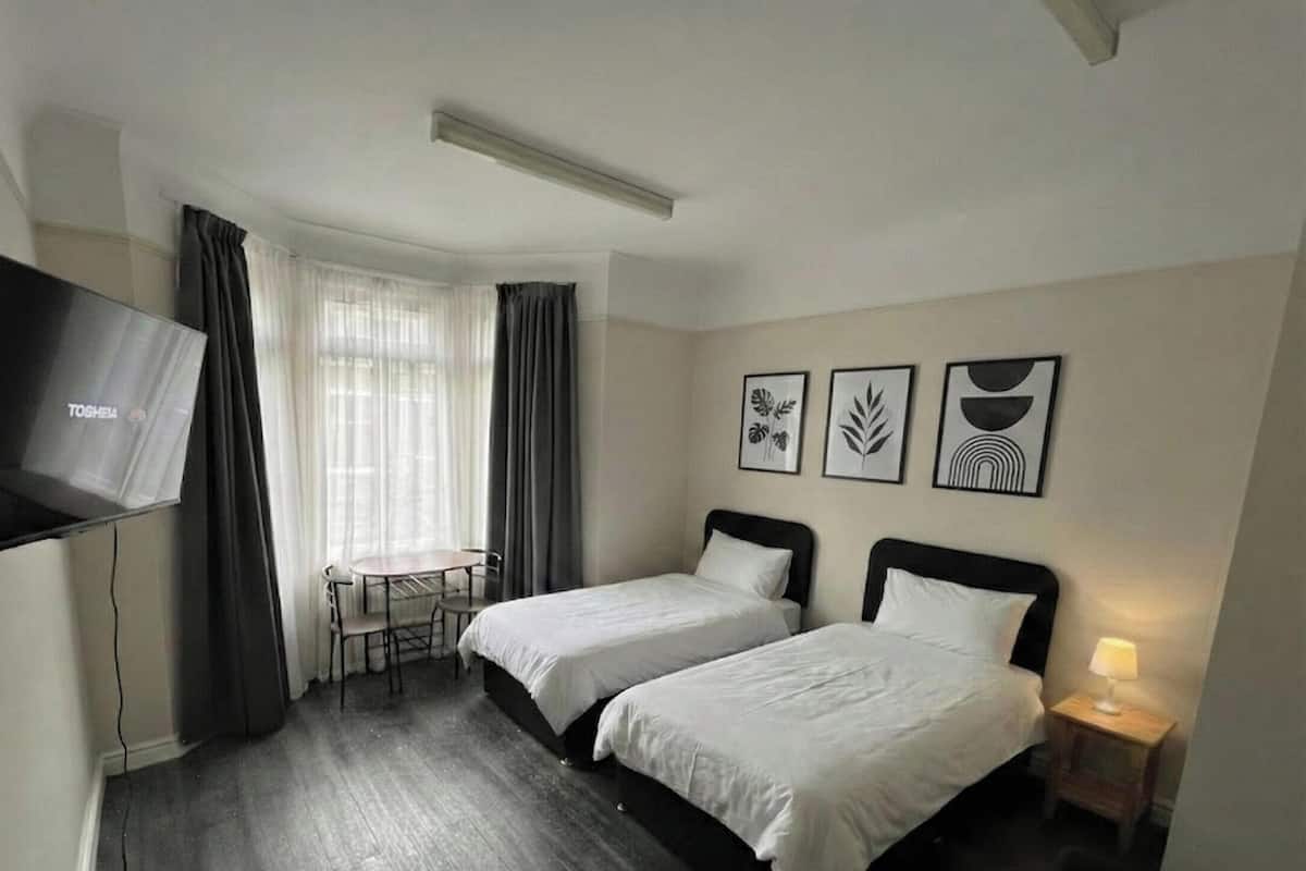 A hotel room with two beds, a TV, a desk with a chair, and three framed pictures on the wall.