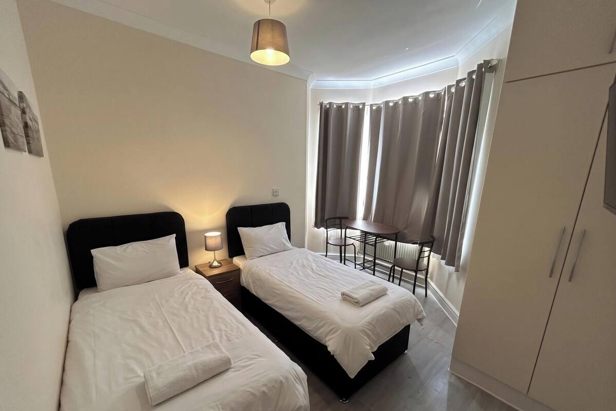 A hotel room with two beds, a desk, a chair, a wardrobe, and a window with curtains.