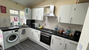 A kitchen with white cabinets, a washing machine, a microwave, a stove, and various kitchen items on the counter. - Gassiot House (London)