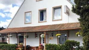 A two-story building with a sloped roof, large windows, and a porch area with potted plants. - Hotel Riede (Bremen)