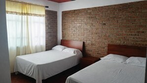 Une chambre avec deux lits simples, un mur en briques et une fenêtre avec des rideaux.