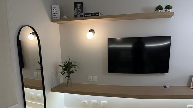 Una sala moderna con un televisor de pantalla plana montado en la pared, una mesa de centro de madera y un espejo grande a la izquierda.