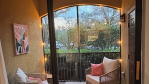 Une pièce dotée d’une porte-fenêtre coulissante donnant sur un balcon extérieur aménagé avec des meubles en osier et des guirlandes lumineuses.