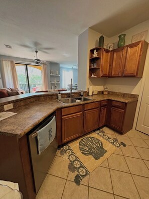 A kitchen with granite countertops, wooden cabinets, a dishwasher, and a patterned rug. - Spacious 2 Bed/2 Bath Condo in Sarasota, Local to Beaches, Shopping, & More (Sarasota)
