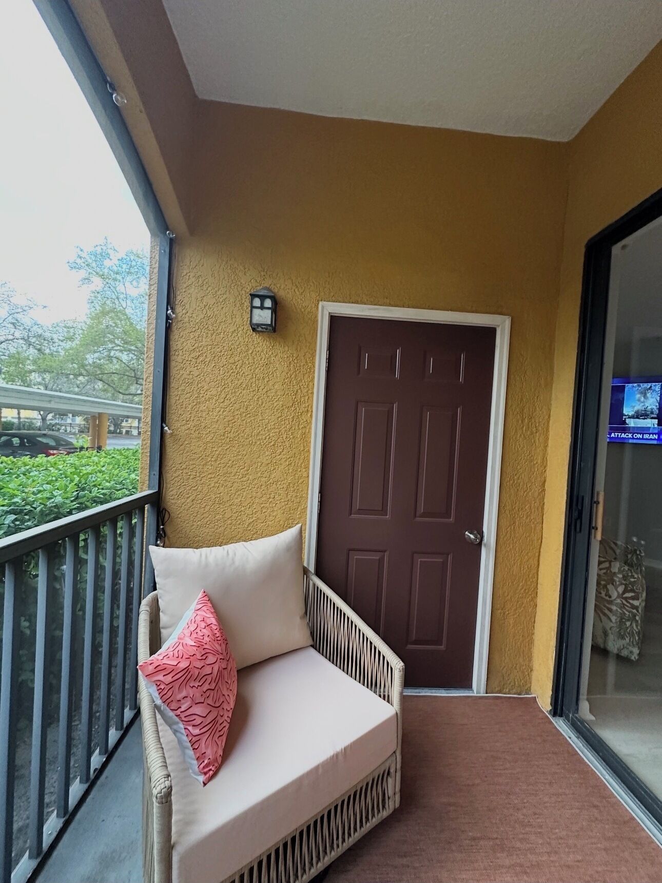 A balcony with a cushioned seating area, a door, and a wall-mounted light fixture.