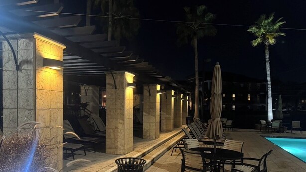 Un espace aménagé au bord de la piscine, avec des chaises longues et des parasols, une structure en colonnes de pierre et une piscine.