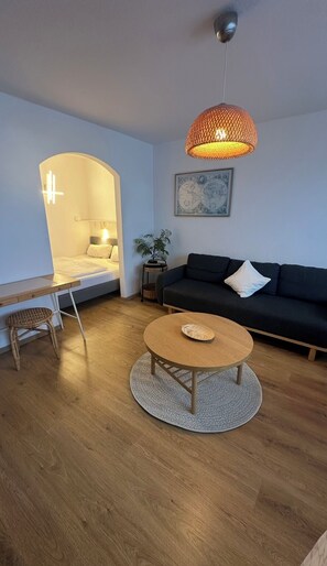 Een moderne woonkamer met een bed, een bank, een ronde salontafel en een hanglamp.