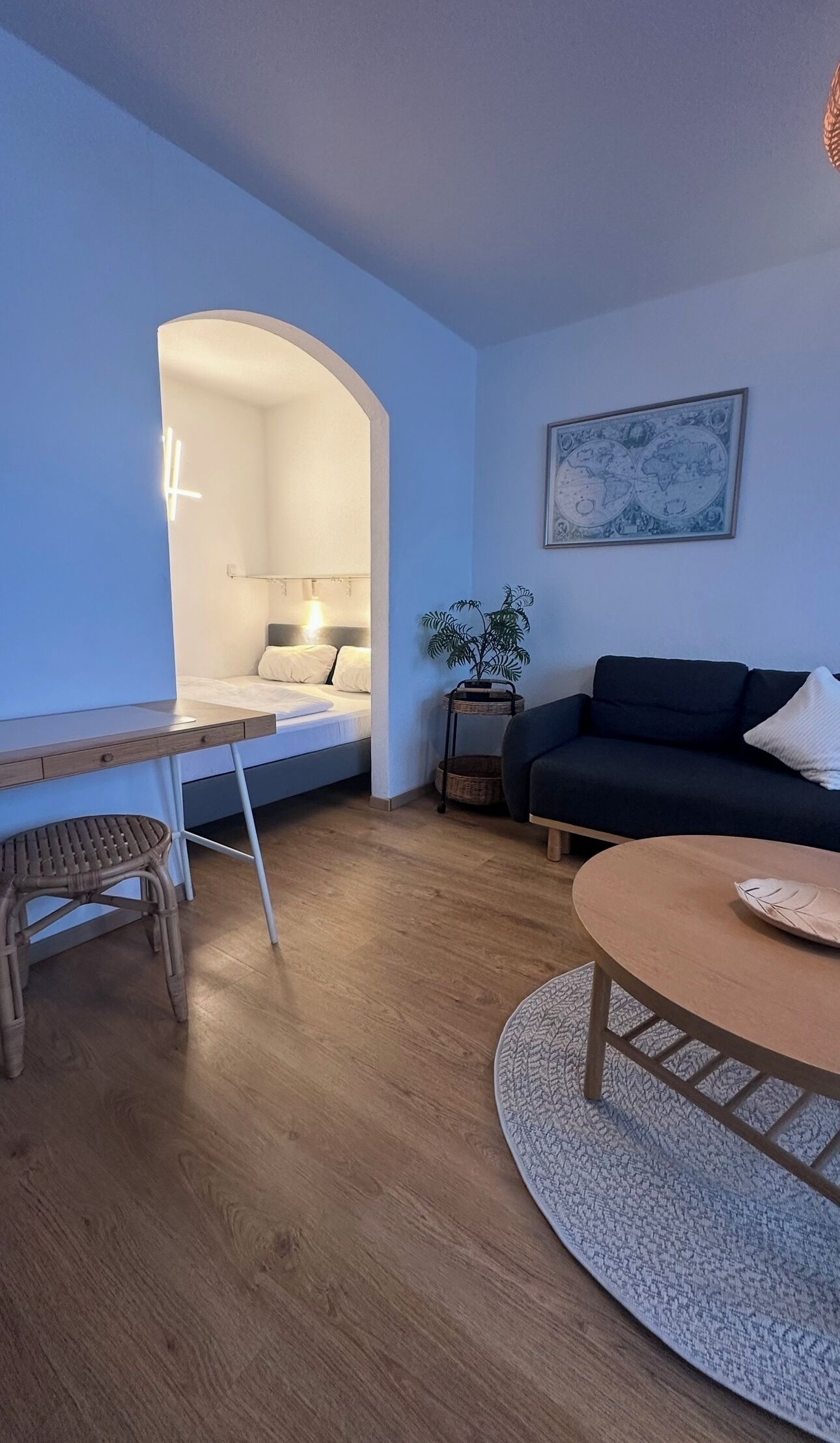 Una sala de estar moderna con una cama, un sofá, una mesa de comedor y una planta pequeña.