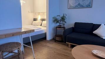 Una sala de estar moderna con una cama, un sofá, una mesa de comedor y una planta pequeña.