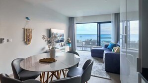 Uma sala de estar moderna com uma mesa de jantar redonda, um sofá e uma varanda com vista para o mar.