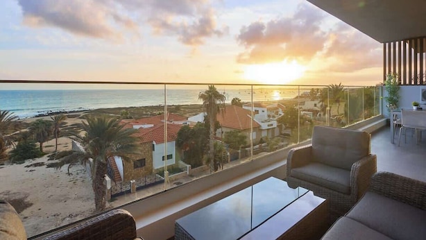 Uma varanda com vista para a praia e o oceano ao pôr do sol.