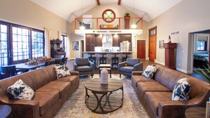 A spacious living area with a high ceiling, a dining table, and a kitchen in the background.