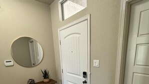 Un couloir avec une console en bois, un miroir rond, une porte blanche et une petite fenêtre au-dessus de la porte.