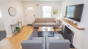 A modern living room with a sofa, a coffee table, a TV, and a fireplace. - Charming Single Family Home - Free 3 car parking (Washington)