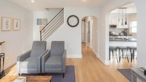 A modern living room with a staircase, a kitchen visible through an archway, and a dining area with bar stools. - Charming Single Family Home - Free 3 car parking (Washington)