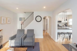 A modern living room with a staircase, a kitchen visible through an archway, and a dining area with bar stools. - Charming Single Family Home - Free 3 car parking (Washington)
